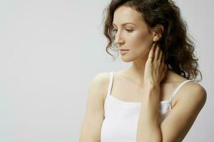 Thoughtful pensive upset curly beautiful woman in basic white t-shirt touches neck looks aside think about work posing isolated on over white background. People Emotions Lifestyle concept. Copy space photo