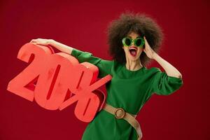 Portrait of a charming lady green dress afro hairstyle dark glasses twenty percent in hands red background unaltered photo