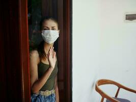 mujer en médico máscara mirando fuera el ventana triste Mira prohibición foto