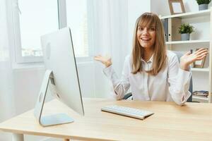 sonriente alegre adorable rubia mujer de negocios trabajador persona de libre dedicación Mira a cámara aumento mano arriba en ligero moderno oficina. contento empleado trabajo en computadora en línea, disfrutar exitoso negocio. Copiar espacio foto