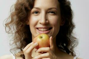 de cerca retrato de alegre linda Rizado hermosa mujer en básico blanco camiseta disfrutar manzana sonriente posando aislado en terminado blanco antecedentes. natural Respetuoso del medio ambiente productos concepto. Copiar espacio foto