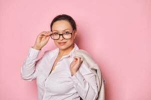 Close-up serious charming brunette holding her hand on her stylish black-rimmed glasses, looking confidently into camera photo