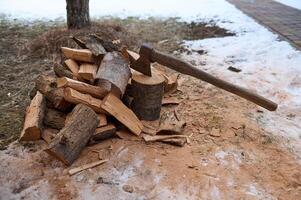 Rustic still life with an old handle axe, a hatchet in stump near firewood against the snowy nature background photo