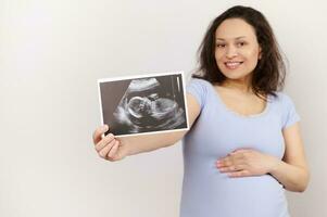 Focus on ultrasound scan image, baby sonography in the hand of a smiling pregnant woman, isolated on white background photo