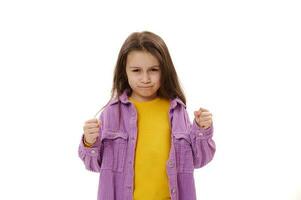 Curious angry little child girl clenching fists, expressing negative emotions and dissatisfaction, looking at camera photo