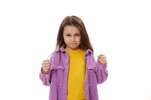 Curious angry little child girl clenching fists, expressing negative emotions and dissatisfaction, looking at camera photo