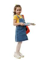 Caucasian smiling excellent student, first grader schoolgirl, holding studying books, going to school, isolated on white photo