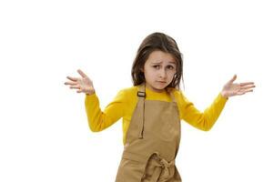 Amazed little child girl in beige chef's apron, asking questions, holding hands palms up, isolated over white background photo