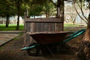 Still life with wheelbarrow standing near compost pit in a garden plot. Zero waste concept. Composting. Sustainability. photo