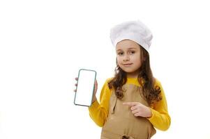 pequeño cocinero confitero en del chef sombrero y delantal, puntos a blanco blanco pantalla de teléfono inteligente, anuncio espacio para móvil aplicaciones foto