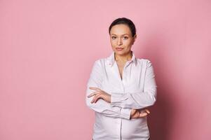 Confident middle aged multi-ethnic pregnant woman in white casual shirt, posing with her arms folded, looking at camera photo