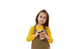 Adorable Caucasian child girl holding disposable paper cup with hot drink, looking at camera, isolated white background photo