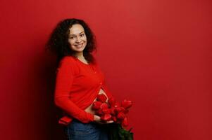 Happy Women's and Mother's Day concept. Beautiful smiling ethnic pregnant woman with red tulips on isolated background photo