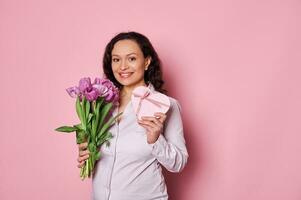 Beautiful pregnant woman holding bouquet of purple tulips and heart shaped gift box with happy present for Mother's Day photo