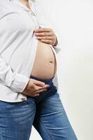 Midsection of pregnant woman holding hands on her bare belly, isolated on white background. Pregnancy 28 weeks photo