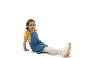 Horizontal full length portrait of Caucasian child girl looking confidently at camera, sitting on white background photo