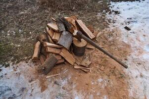 parte superior ver hacha o Madera quemandose hacha pega en un tocón cerca un montón de leña, haciendo fuego en un nieve cubierto bosque foto