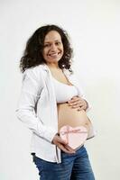 Happy woman future mom caresses belly, smiles at camera, shows heart shaped gift box with happy present for Mother's Day photo