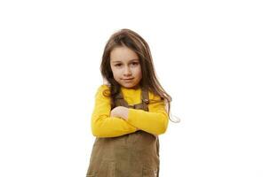 retrato de un sonriente pequeño Chica de escuela en pie con manos doblada, sonriente mirando a cámara, aislado blanco antecedentes foto