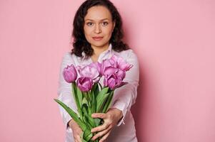 Details  beautiful purple tulips in hands of charming woman holding out at camera a bouquet for festive occasion photo