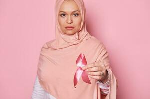 pecho cáncer conciencia rosado cinta, en manos de borroso musulmán mujer en rosado hiyab, demostración apoyo para cáncer pacientes foto