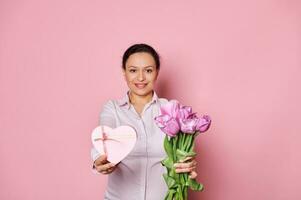 Middle-aged pretty woman holding out at camera a bouquet of tulips and heart shaped gift box, greeting with Mother's Day photo