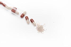 Still life. View from above of enteric capsules spilling out from gel translucent capsule, scattered on white background photo