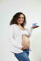 Smiling excited pregnant woman holding blue knitted baby booties, caressing belly, isolated over white background photo