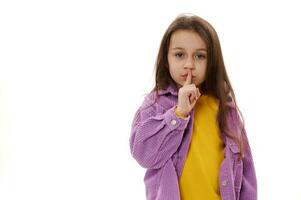 Caucasian little girl puts index finger on her lips, shows silence sign, looking at camera, isolated on white background photo