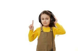 adorable sonriente pequeño niña vistiendo auriculares para en línea educación o distancia aprendiendo, señalando dedo a Copiar espacio foto