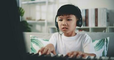 Mano disparo, creativo asiático chico vistiendo auricular con artístico habilidades tomando música lecciones en línea durante un vídeo llamada y jugando el piano a hogar. música, pasatiempo y estilo de vida conceptos. video