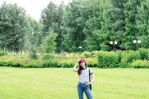 a girl in a gray T-shirt and a red cap on a background of greenery, in the park, copy space photo