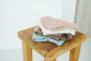 Stack of cotton tops in natural tones on wooden chair in bright room photo