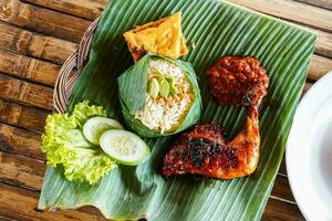 Grilled chicken with red barbecue sauce, vegetables and chili sauce served on banana leaves photo