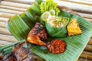 Grilled chicken with red barbecue sauce, vegetables and chili sauce served on banana leaves photo