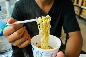 instant noodles, noodle soup in a cup, boys hand feeding ready to eat noodles photo