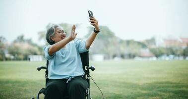 Mature Asian woman on wheelchair use smartphone make video call photo