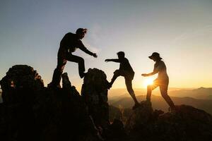 Silhouette of Hikers climbing up mountain cliff.  Concept of help and teamwork, Climbing group helping each other while climbing up in sunset. Limits of life and Hiking success full. photo