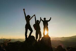 Silhouette of happy teamwork with success gesture standing on the top of mountain, business teamwork concept, business victory, achieve business goal. photo