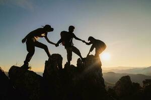 silhouette of Teamwork of three  hiker helping each other on top of mountain climbing team. Teamwork friendship hiking help each other trust assistance silhouette in mountains, sunrise. photo