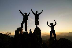 Silhouette of happy teamwork with success gesture standing on the top of mountain, business teamwork concept, business victory, achieve business goal. photo