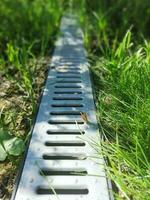 drainage systems. metal construction from the roof - sewer and grate on the ground for draining water closeup. sunny day, green grass photo