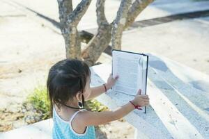 Side view of asian girl sitting on a bench and reading a book in the park. photo