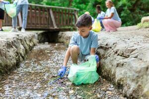 Kid boy handpicking gathering up garbage plastic straws garbage from the river at the park. World environment day.Environment concept. photo