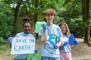 diverso grupo de personas cosecha arriba basura en el parque voluntario comunidad servicio. contento internacional voluntarios participación cartel con 'ahorrar el tierra' mensaje. foto