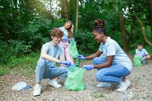 Happy community service people cleaning up local park. They have a trash bag and are filling is with trash they have found in the park. Their are two knealing down and others behind them photo