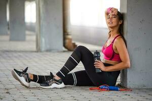 Fitness woman Relaxing after exercise with a whey protein bottle. Relaxing after training. Beautiful young woman looking away while resting after running photo