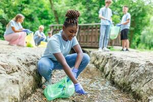 Woman handpicking gathering up garbage plastic straws garbage from the river at the park. World environment day.Environment concept. photo