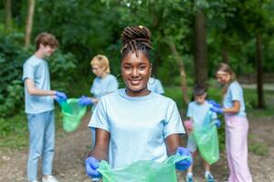 Portrait of beautiful woman with small group of volunteers on background with gloves and garbage bags cleaning up city park - environment preservation and ecology concept. All wearing a blue t-shirts photo