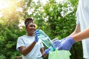 Two smiling diverse young male volunteers putting trash in garbage bags during a community cleanup day in a field photo